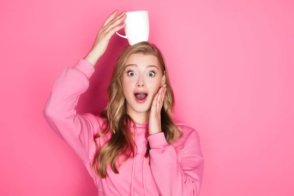 ピンクを背景に口を開けてマグカップを持つ衝撃的な美しい女性 — ストック写真