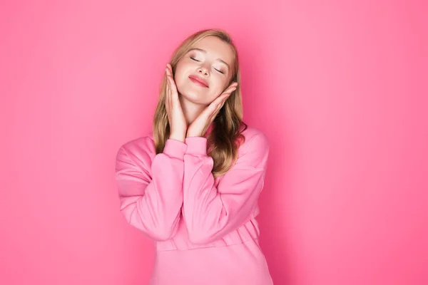 ピンクの背景で目を閉じて笑顔でパーカーの美しい若い女性 — ストック写真