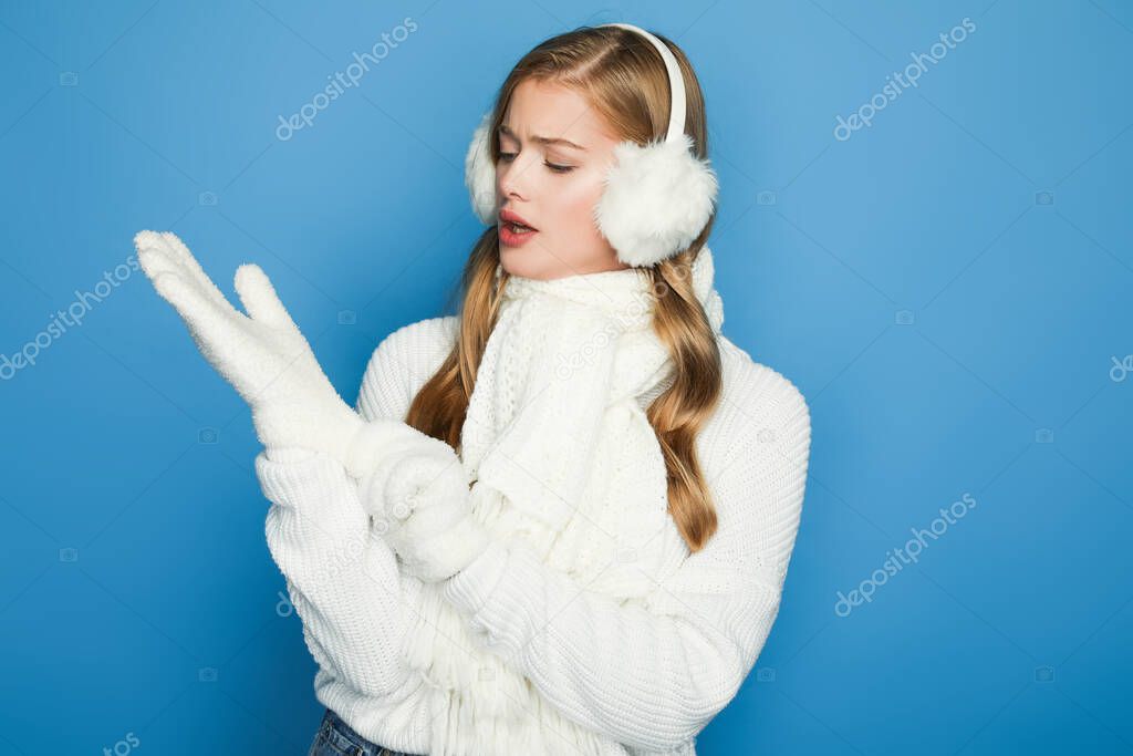 beautiful woman in winter white outfit putting gloves on isolated on blue