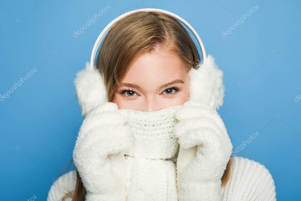 beautiful woman in winter white outfit covering face with scarf isolated on blue