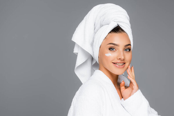 smiling woman with towel on head and cosmetic cream on face isolated on grey