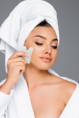 Kafasında havlu olan kadın gri üzerine gua sha kullanıyor.