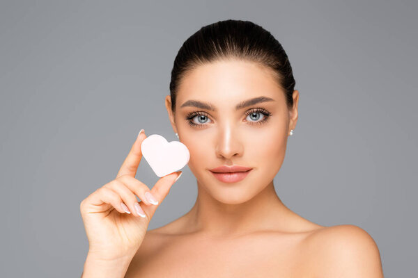 женщина с обнаженными плечами и сердцем в форме косметической губки, изолированной на сером