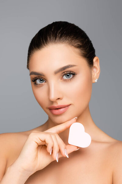 женщина с обнаженными плечами и сердцем в форме косметической губки, изолированной на сером