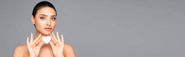 женщина с обнаженными плечами и сердечной формы косметическая губка изолирована на сером, баннер