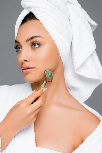 头戴毛巾的女人用翡翠滚筒把脸隔离在灰色上 — 图库照片