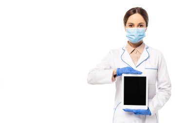 Lateks eldivenli ve tıbbi maskeli doktor beyaz ekranlı dijital tableti gösteriyor.
