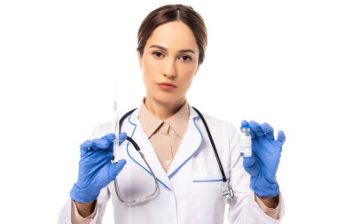 Beyaz kameraya bakarken elinde şırınga ve aşı tutan lateks eldivenli doktor.