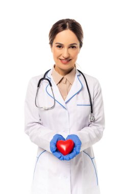 Lateks eldivenli gülümseyen doktor, kırmızı kalbi beyazın üstünde tutuyor.
