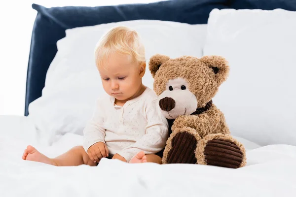 選択的焦点の幼児座って近く柔らかいおもちゃオンベッド上の白い背景 — ストック写真