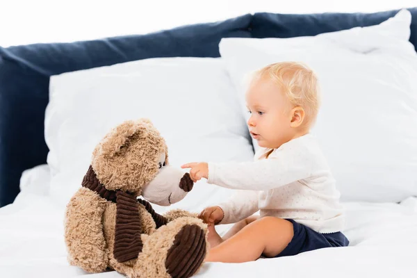 幼児男の子Pointingで柔らかいおもちゃオンベッド上の白い背景 — ストック写真