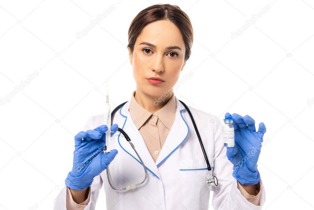 Doctor in latex gloves holding syringe and vaccine while looking at camera isolated on white