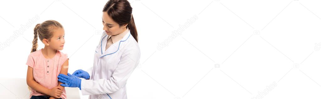 Panoramic shot of doctor in latex gloves touching hand of girl with patch isolated on white