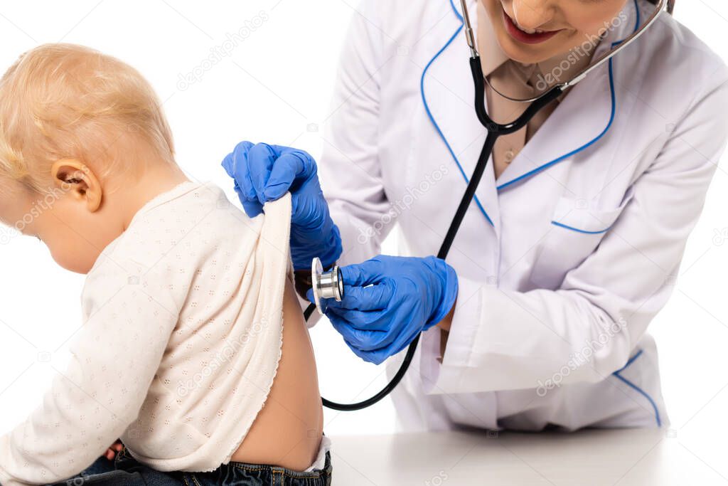 Smiling pediatrician examining back of toddler boy with stethoscope isolated on white