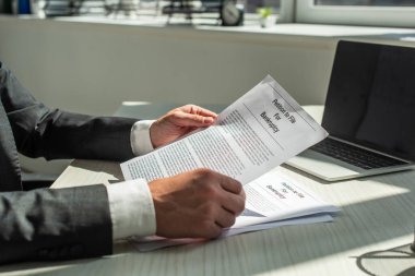 Cropped view of businessman holding petition for bankruptcy, while sitting at workplace on blurred background clipart