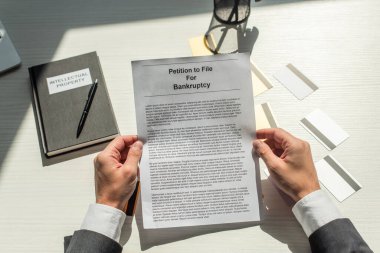 Cropped view of businessman holding petition for bankruptcy near credit cards and notebook on white textured background clipart