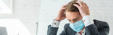 Businessman in medical mask holding hands near head with blurred flipchart on background, banner clipart