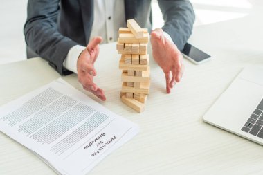 Cropped view of bankrupt with hands near blocks wood tower game, sitting at workplace clipart
