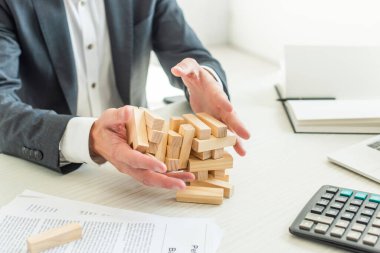 Kırpılmış iş adamı görüşü blokları ahşap oyun çöküşü, iş yerinde belgelerin yanında otururken 