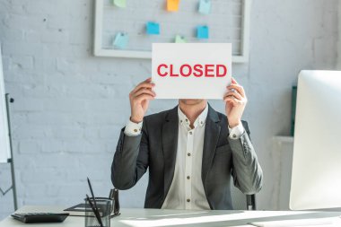 Businessman holding sign with closed lettering, while sitting at workplace clipart