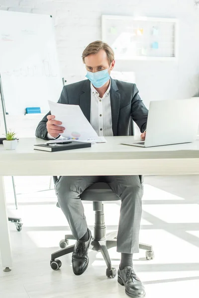 Full Length Businessman Medical Mask Looking Paper While Sitting Table — Stock Photo, Image