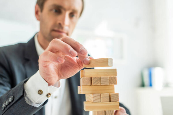 Concentrated businessman playing blocks wood game on blurred background