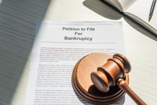 Gavel with wooden block on petition for bankruptcy near blank notebook on white textured background