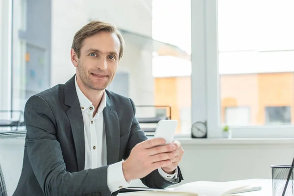 Positive Businessman Smartphone Looking Camera While Siting Workplace Blurred Window — Stock Photo, Image