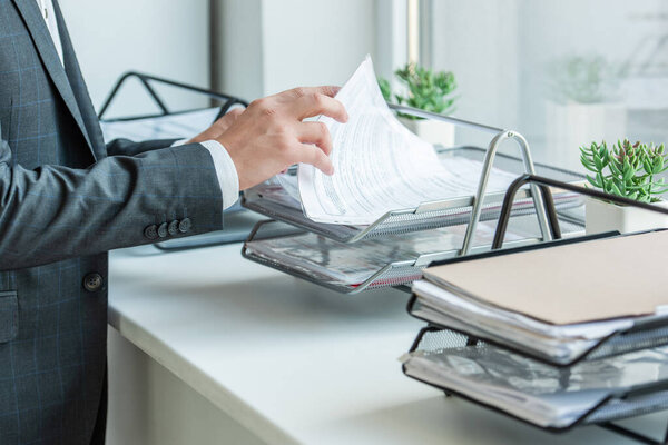 Обрезанный вид бизнесмена, ищущего бумагу в лотке для документов, стоя у окна