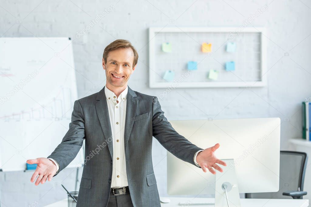 Front view of happy businessman with open arms looking at camera with blurred office on background