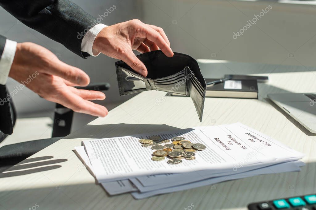 Cropped view of businessman holding empty wallet near coins on petitions for bankruptcy on table