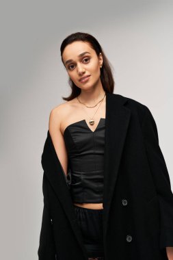 Esmer model, bir stüdyoya zarafet ve güven saçan modaya uygun siyah giysiler sergiliyor..