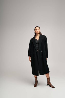 Esmer kadın modern bir stüdyo alanına güvenerek şık siyah kıyafetler sergiliyor..