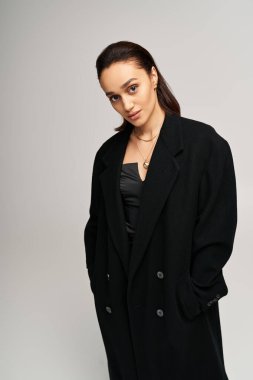 Esmer güzellik zarif bir şekilde siyah bir paltoyla poz veriyor. Stüdyoda bir korsenin üzerine yerleştirilmiş..