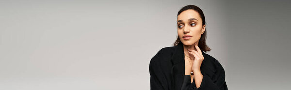 Молодая женщина в шикарном черном ансамбле изящно позирует в сложной студийной обстановке, баннер