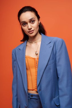 Güzel genç bir kadın turuncu korseli şık mavi bir takım elbiseyle rahatça poz veriyor..