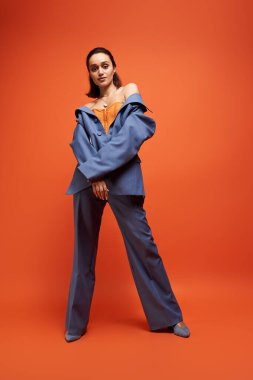 Genç bir kadın şık bir stüdyoda turuncu korseli modaya uygun mavi bir takım modellik yapıyor..