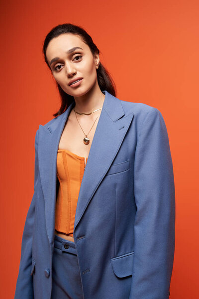 Модель брюнетки демонстрирует модный синий костюм и корсет на оранжевом фоне.