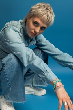 Güzel ve şık genç bir kadın, neşeli bir poz verirken kot elbisesini sergiliyor..