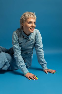 Kot pantolon giymiş hoş bir kadın rahat bir anın tadını çıkarıyor. Neşeli bir gülümsemeyle canlı tırnak sanatı sergiliyor..