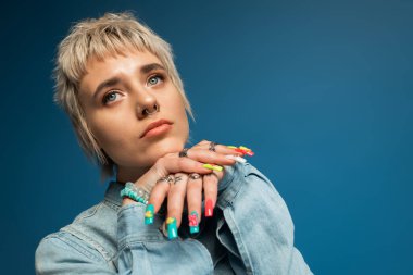 Büyüleyici genç kadın renkli tırnaklarını ve moda tarzını düşünceli bir ifadeyle sergiliyor.
