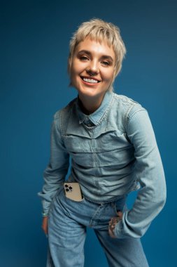 Kendine güvenen genç bir kadın neşeyle poz veriyor, modaya uygun kıyafetlerini ve çarpıcı özelliklerini sergiliyor..