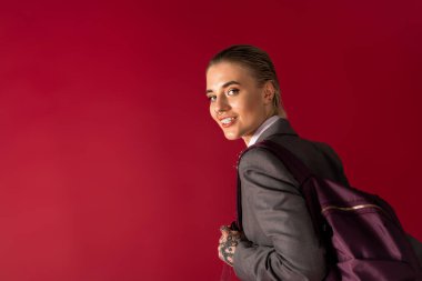 Moda bir sırt çantasıyla şık genç bir kadın parlak kırmızı bir arka planda parlıyor.