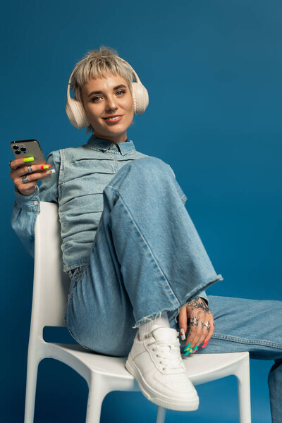 Bright eyed woman with trendy outfit smiles while listening to music on headphones, radiating joy.