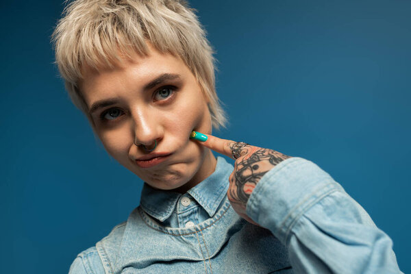 Beautiful young woman in denim shirt displays a playful expression with vibrant nails.