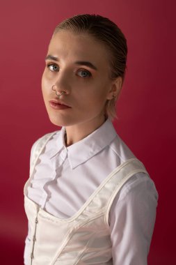 Güzel bir kadın şık bir kıyafetle kendinden emin bir şekilde poz verir, bakışları kırmızı bir duvara karşı büyüleyicidir..