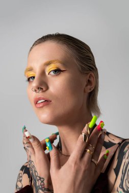 Cesur makyajlı, renkli tırnaklı ve kendinden emin bir duruşu olan genç bir kadın..