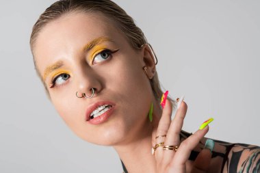 Çarpıcı özellikleri olan genç bir kadın yaratıcı bir duruşta cesur makyaj ve renkli tırnaklar sergiliyor..