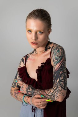 Genç bir kadın kendine güvenerek poz veriyor, dövmeleri ve eşsiz kıyafetleri cesur tarzını sergiliyor..