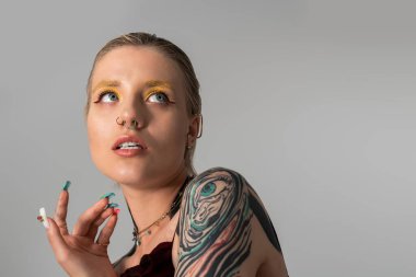 Genç bir kadın kendine özgü stilini canlı bir makyajla, dövmelerle ve büyüleyici bir ifadeyle sergiliyor..